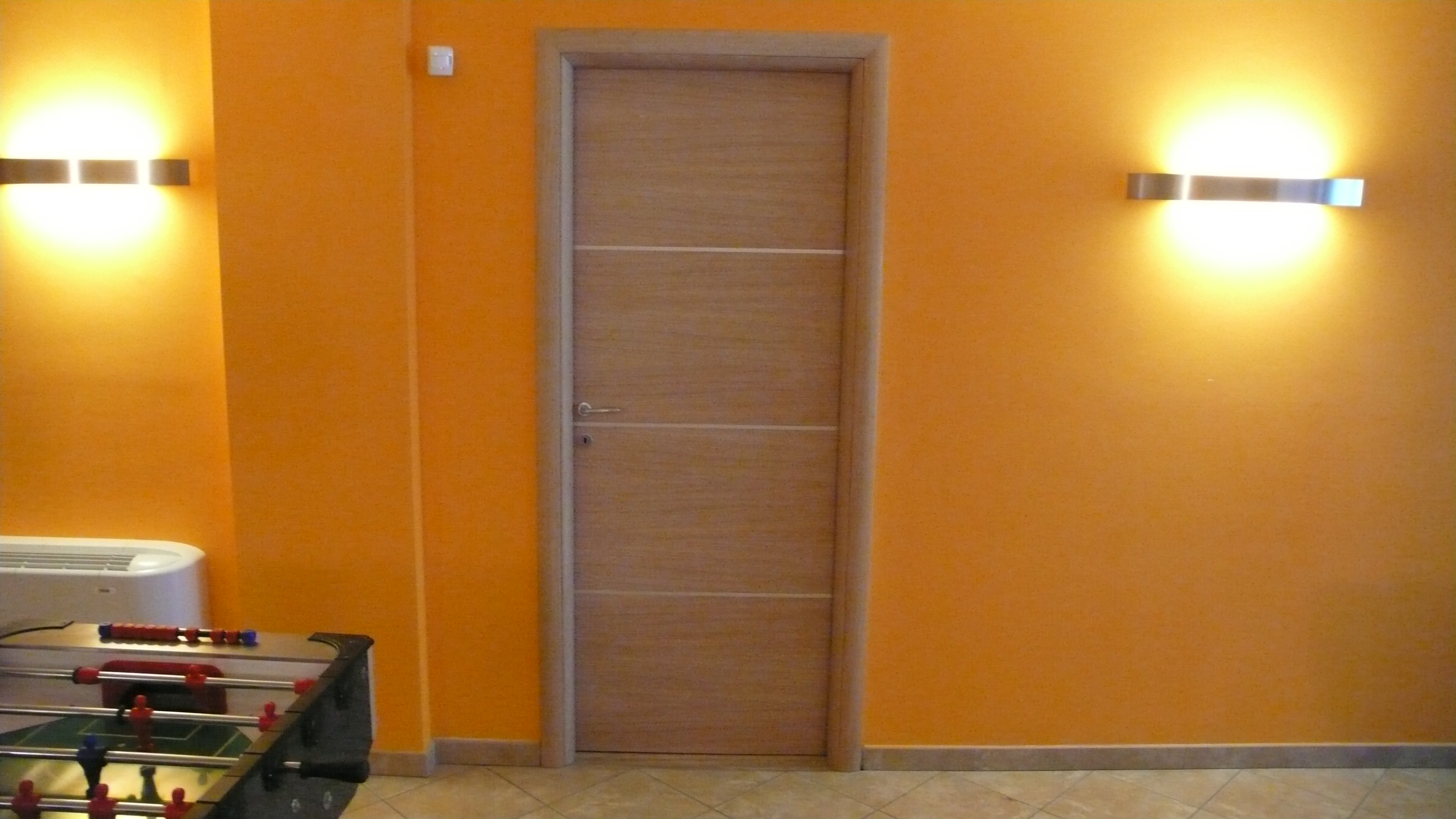 Porta in legno chiaro su parete arancione.