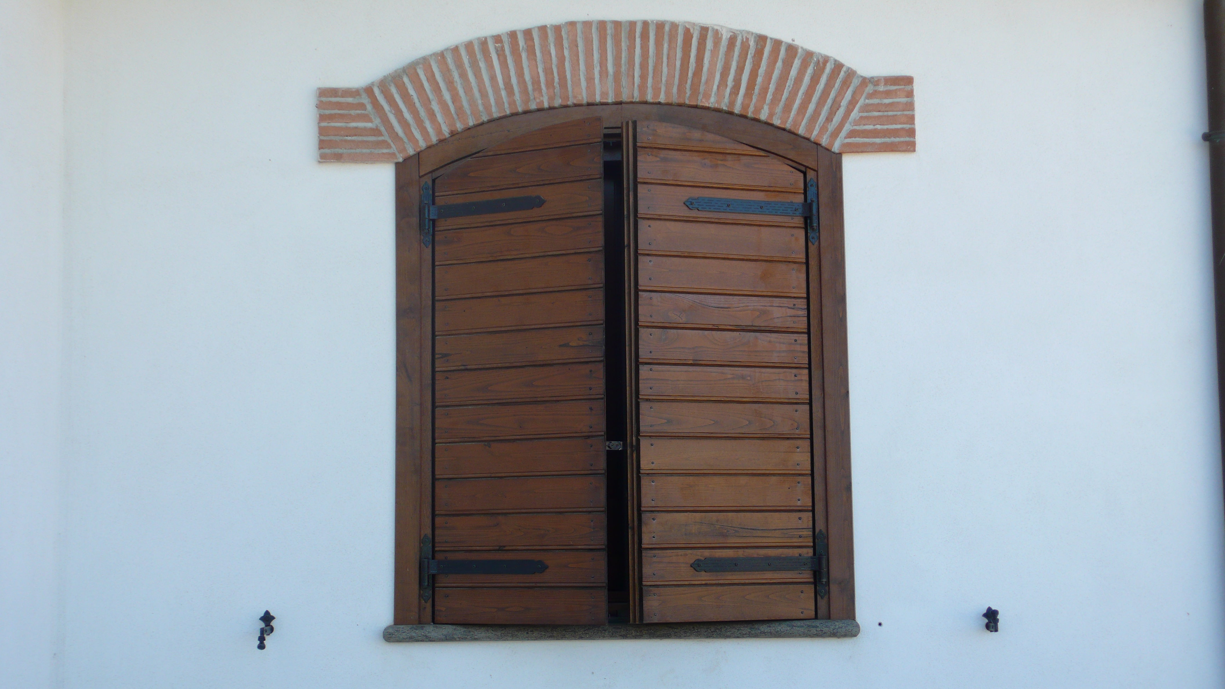 Finestra con persiane in legno chiuse, muro bianco.