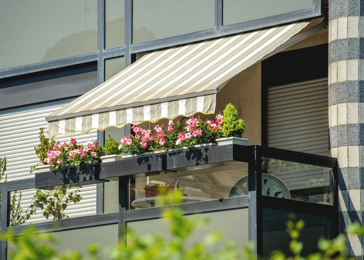 Balcone con tenda a righe e fiori rosa.