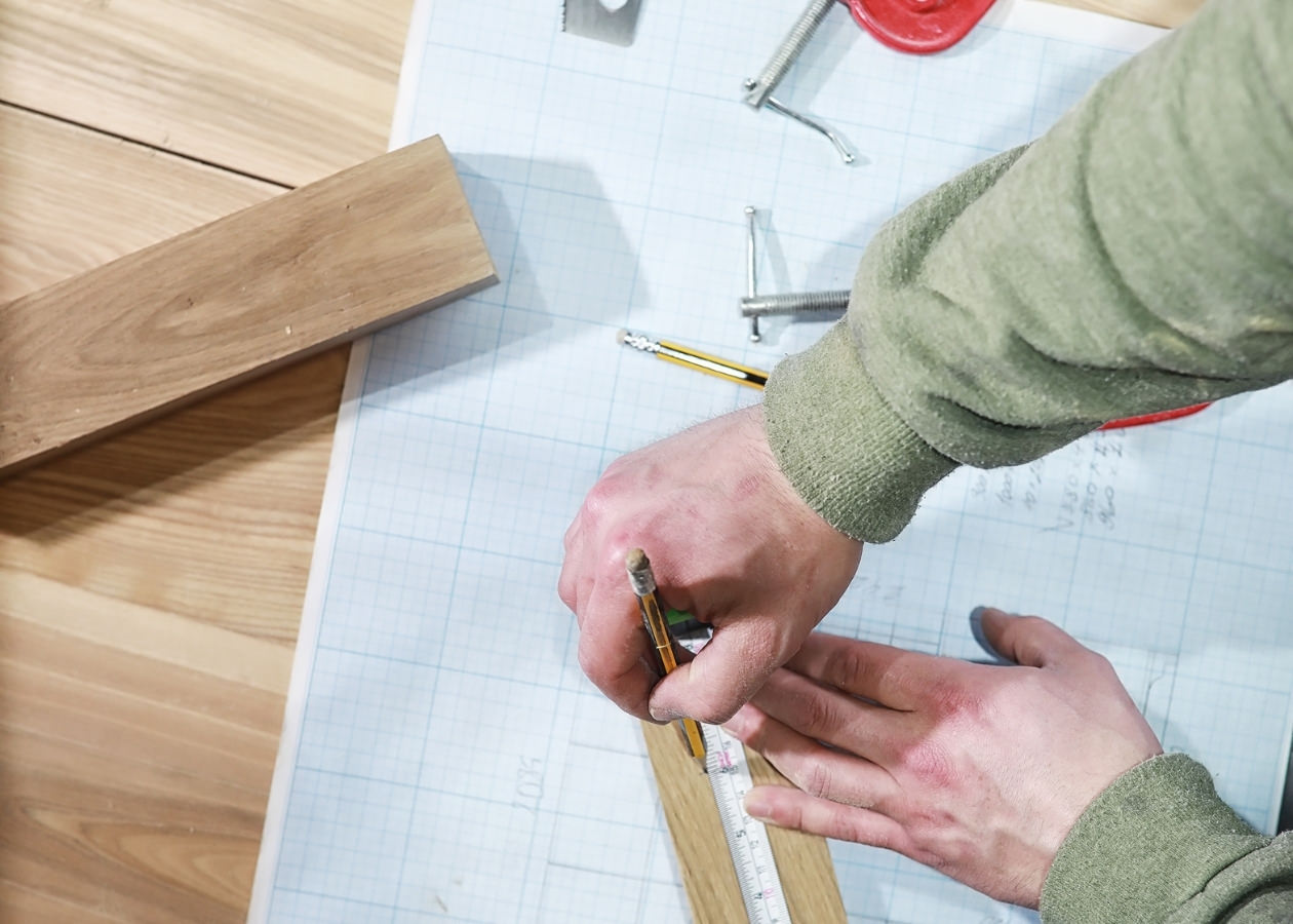 Mani che misurano legno su carta millimetrata.