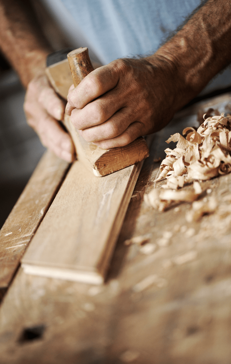 Mani che piallano un pezzo di legno.